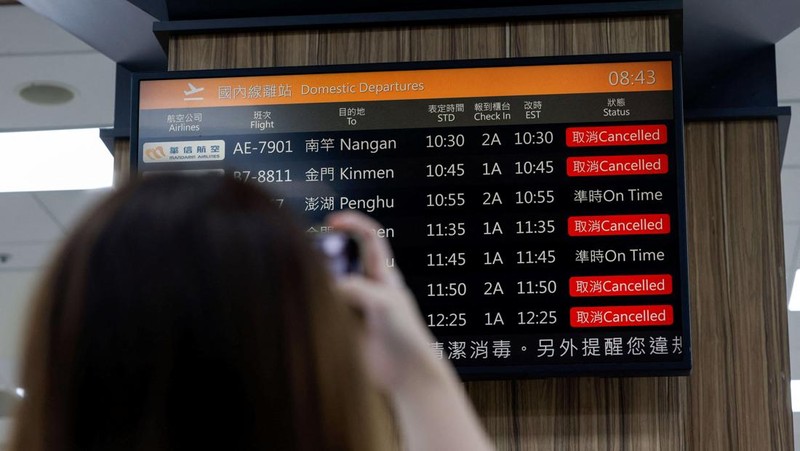 A person takes a photo of a flight information display screen that shows cancelled flights at the Taipei Songshan Airport, as China conducts 
