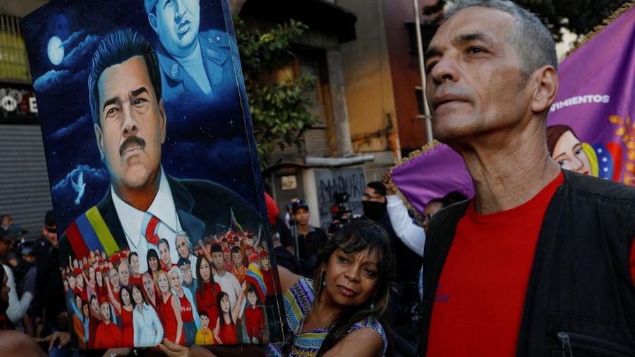 Seorang pendukung Presiden Venezuela Nicolas Maduro memegang lukisan dirinya dan mendiang Presiden Hugo Chavez, selama pawai yang menyerukan pembebasan Maduro, setelah ia dan istrinya Cilia Flores ditangkap menyusul serangan AS di Venezuela, di Caracas, Venezuela, 4 Januari 2026. (REUTERS/Fausto Torrealba)