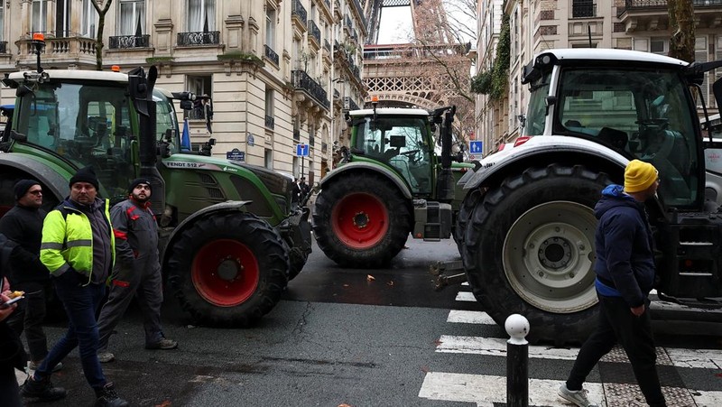 Orang-orang berjalan di samping traktor yang memblokir jalan di dekat Menara Eiffel, saat para petani Prancis memprotes penanganan pemerintah terhadap perjanjian perdagangan bebas Uni Eropa-Mercosur dan penanganan wabah penyakit kulit berbenjol, di Paris, Prancis, 8 Januari 2026. (REUTERS/Gonzalo Fuentes)
