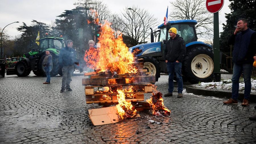 Orang-orang berjalan di samping traktor yang memblokir jalan di dekat Menara Eiffel, saat para petani Prancis memprotes penanganan pemerintah terhadap perjanjian perdagangan bebas Uni Eropa-Mercosur dan penanganan wabah penyakit kulit berbenjol, di Paris, Prancis, 8 Januari 2026. (REUTERS/Gonzalo Fuentes)