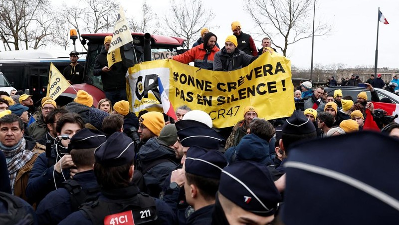 Orang-orang berjalan di samping traktor yang memblokir jalan di dekat Menara Eiffel, saat para petani Prancis memprotes penanganan pemerintah terhadap perjanjian perdagangan bebas Uni Eropa-Mercosur dan penanganan wabah penyakit kulit berbenjol, di Paris, Prancis, 8 Januari 2026. (REUTERS/Gonzalo Fuentes)