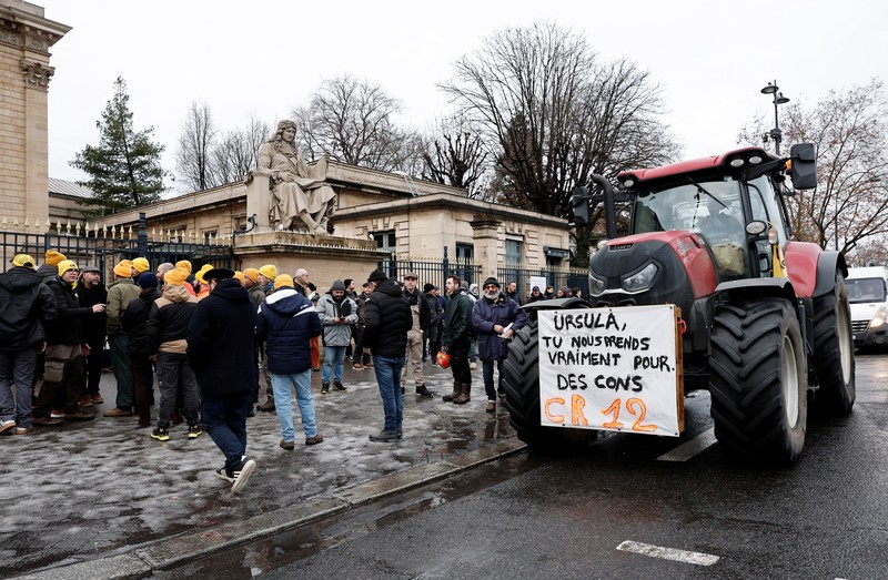 Orang-orang berjalan di samping traktor yang memblokir jalan di dekat Menara Eiffel, saat para petani Prancis memprotes penanganan pemerintah terhadap perjanjian perdagangan bebas Uni Eropa-Mercosur dan penanganan wabah penyakit kulit berbenjol, di Paris, Prancis, 8 Januari 2026. (REUTERS/Gonzalo Fuentes)
