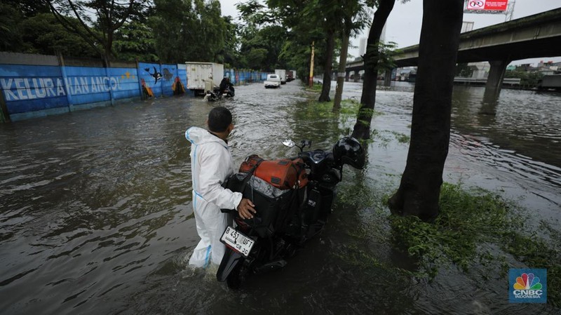 Pengendara sepeda motor melewati banjir di depan pintu masuk Taman Impian Jaya Ancol (pintu barat)di Pademangan, Jakarta, Senin (12/1/2026). (CNBC Indonesia/Tri Susilo)