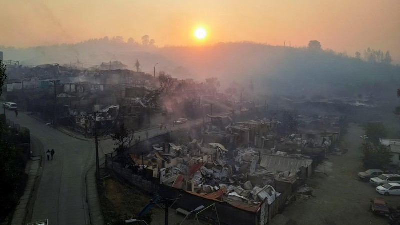A car drives as fire and smoke rise from a forest fire in the Biobio region where, according to local media, multiple wildfires prompted emergency evacuations, in Concepcion, Chile, January 18, 2026. REUTERS/Juan Gonzalez     TPX IMAGES OF THE DAY