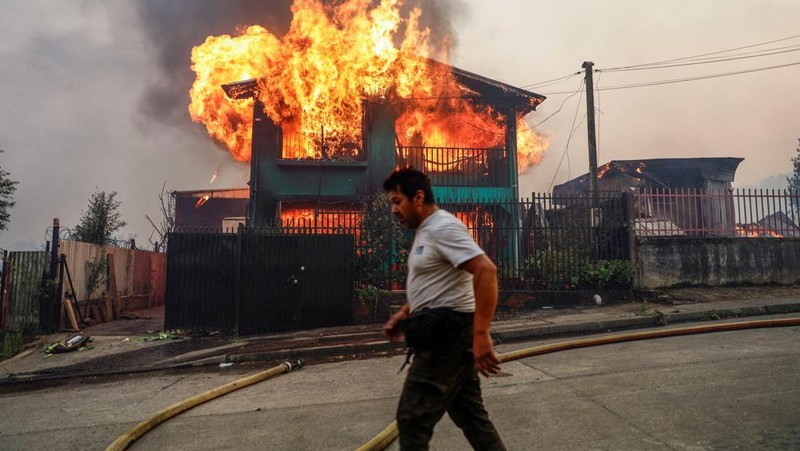 A car drives as fire and smoke rise from a forest fire in the Biobio region where, according to local media, multiple wildfires prompted emergency evacuations, in Concepcion, Chile, January 18, 2026. REUTERS/Juan Gonzalez     TPX IMAGES OF THE DAY