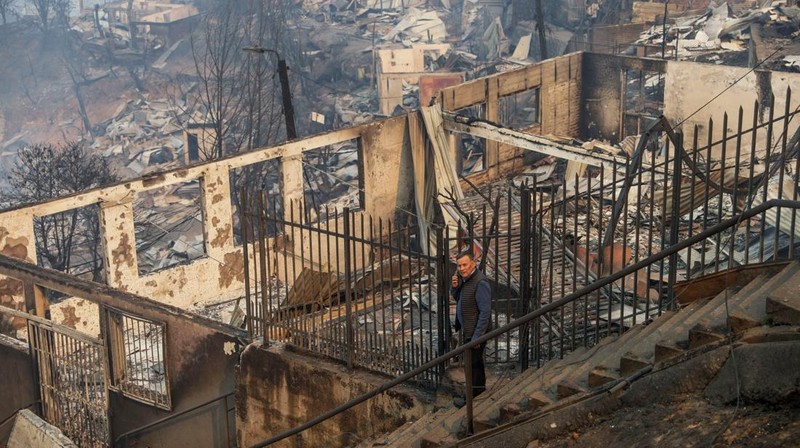 A car drives as fire and smoke rise from a forest fire in the Biobio region where, according to local media, multiple wildfires prompted emergency evacuations, in Concepcion, Chile, January 18, 2026. REUTERS/Juan Gonzalez     TPX IMAGES OF THE DAY