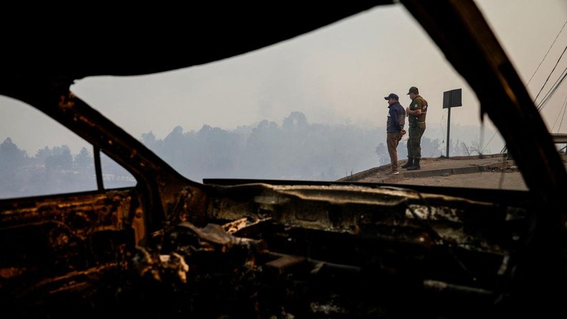 A car drives as fire and smoke rise from a forest fire in the Biobio region where, according to local media, multiple wildfires prompted emergency evacuations, in Concepcion, Chile, January 18, 2026. REUTERS/Juan Gonzalez     TPX IMAGES OF THE DAY
