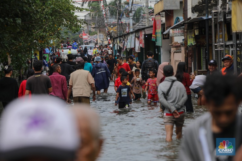 Warga melintasi banjir yang melanda pemukiman penduduk di Kawasan Taman Kota, Kedaung Kali Angke, Jakarta Barat, Jumat (23/1/2026). (CNBC Indonesia/Faisal Rahman)