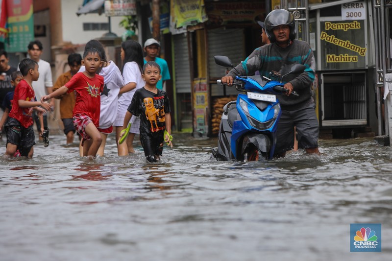 Warga melintasi banjir yang melanda pemukiman penduduk di Kawasan Taman Kota, Kedaung Kali Angke, Jakarta Barat, Jumat (23/1/2026). (CNBC Indonesia/Faisal Rahman)
