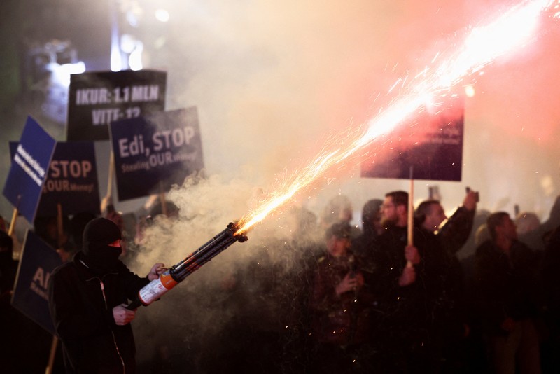 Seorang demonstran menyalakan kembang api di luar kantor Perdana Menteri selama protes anti-pemerintah yang dipicu oleh penyelidikan korupsi terhadap Wakil Perdana Menteri Belinda Balluku, di Tirana, Albania, 24 Januari 2026. (REUTERS/Florion Goga)