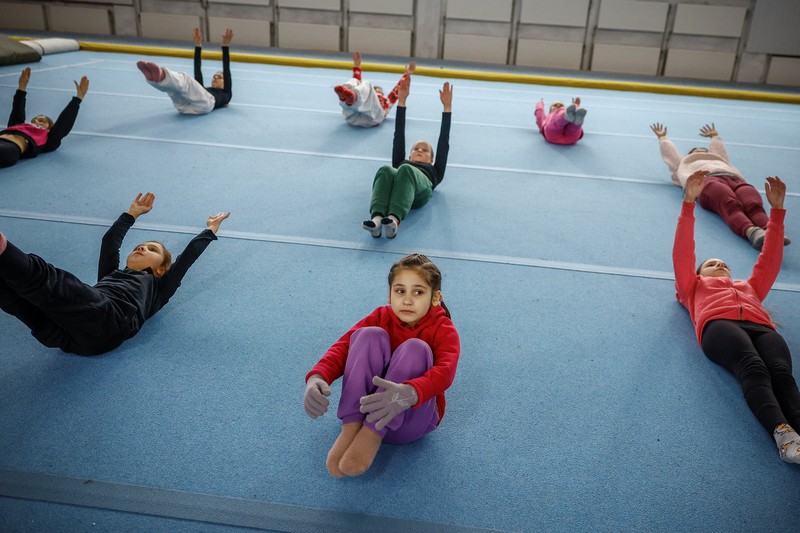 Gadis-gadis yang mengenakan kaus kaki hangat dan pakaian musim dingin berlapis-lapis mengikuti latihan kekuatan selama sesi pelatihan di aula senam di Kiev, Ukraina, Kamis (29/1/2026). (REUTERS/Alina Smutko)