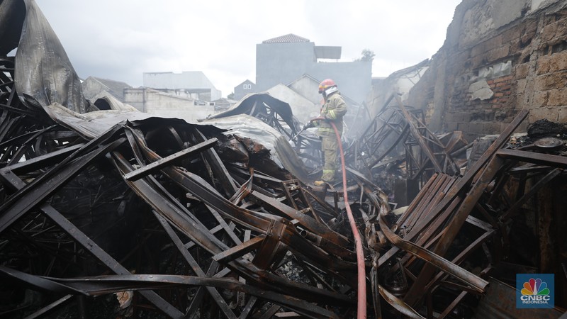 Petugas pemadam kebakaran mendinginkan sisa-sisa api yang masih menyala di Gudang dekorasi dan ruko tekstil di Jalan Pajak Raya, Cipadu, Juramangu Timur, Tangerang Selatan (Tangsel), Senin (2/1/2026). (CNBC Indonesia/Tri Susilo)