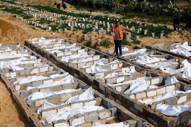 A man gestures next to bodies placed in graves during a mass burial of unidentified Palestinians, whose bodies were released after being held in Israel during the war, in Deir Al-Balah, in the central Gaza Strip, February 13, 2026. REUTERS/Mahmoud Issa