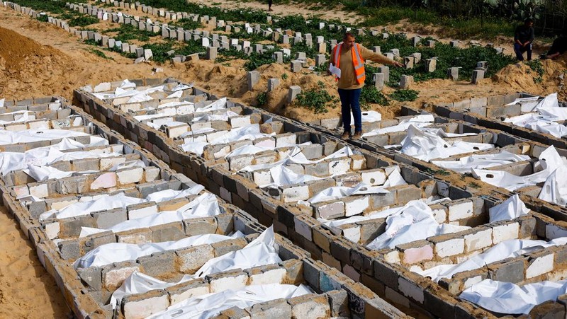 A man gestures next to bodies placed in graves during a mass burial of unidentified Palestinians, whose bodies were released after being held in Israel during the war, in Deir Al-Balah, in the central Gaza Strip, February 13, 2026. REUTERS/Mahmoud Issa
