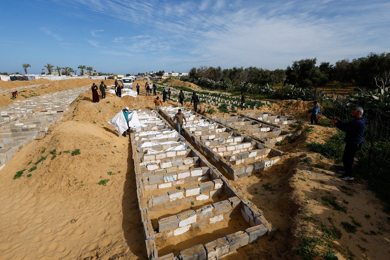 A man gestures next to bodies placed in graves during a mass burial of unidentified Palestinians, whose bodies were released after being held in Israel during the war, in Deir Al-Balah, in the central Gaza Strip, February 13, 2026. REUTERS/Mahmoud Issa
