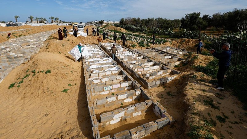 A man gestures next to bodies placed in graves during a mass burial of unidentified Palestinians, whose bodies were released after being held in Israel during the war, in Deir Al-Balah, in the central Gaza Strip, February 13, 2026. REUTERS/Mahmoud Issa