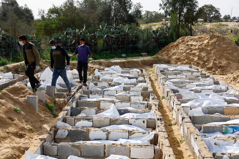 A man gestures next to bodies placed in graves during a mass burial of unidentified Palestinians, whose bodies were released after being held in Israel during the war, in Deir Al-Balah, in the central Gaza Strip, February 13, 2026. REUTERS/Mahmoud Issa