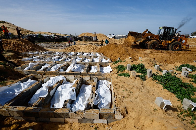 A man gestures next to bodies placed in graves during a mass burial of unidentified Palestinians, whose bodies were released after being held in Israel during the war, in Deir Al-Balah, in the central Gaza Strip, February 13, 2026. REUTERS/Mahmoud Issa