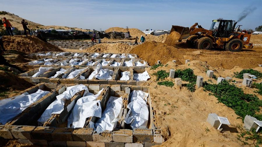 A man gestures next to bodies placed in graves during a mass burial of unidentified Palestinians, whose bodies were released after being held in Israel during the war, in Deir Al-Balah, in the central Gaza Strip, February 13, 2026. REUTERS/Mahmoud Issa