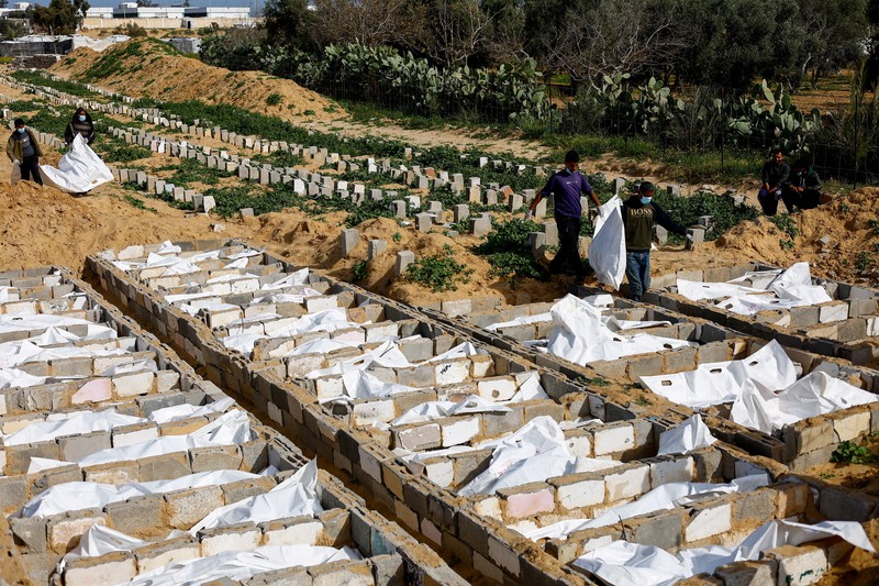 A man gestures next to bodies placed in graves during a mass burial of unidentified Palestinians, whose bodies were released after being held in Israel during the war, in Deir Al-Balah, in the central Gaza Strip, February 13, 2026. REUTERS/Mahmoud Issa