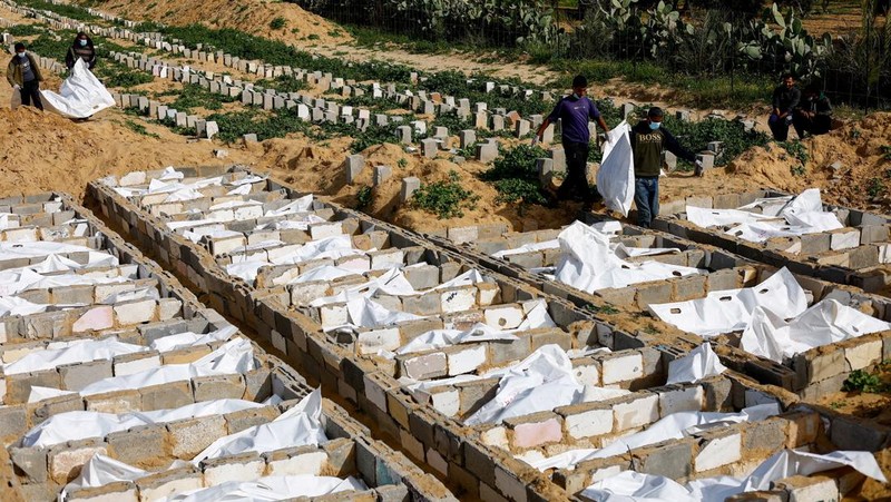A man gestures next to bodies placed in graves during a mass burial of unidentified Palestinians, whose bodies were released after being held in Israel during the war, in Deir Al-Balah, in the central Gaza Strip, February 13, 2026. REUTERS/Mahmoud Issa