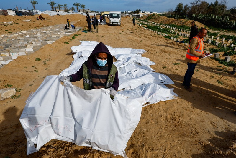A man gestures next to bodies placed in graves during a mass burial of unidentified Palestinians, whose bodies were released after being held in Israel during the war, in Deir Al-Balah, in the central Gaza Strip, February 13, 2026. REUTERS/Mahmoud Issa