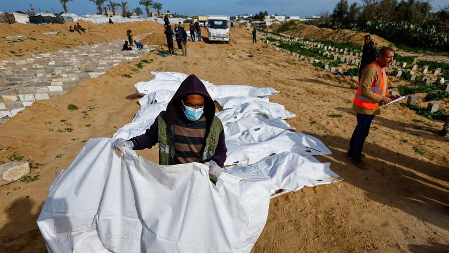 A man gestures next to bodies placed in graves during a mass burial of unidentified Palestinians, whose bodies were released after being held in Israel during the war, in Deir Al-Balah, in the central Gaza Strip, February 13, 2026. REUTERS/Mahmoud Issa