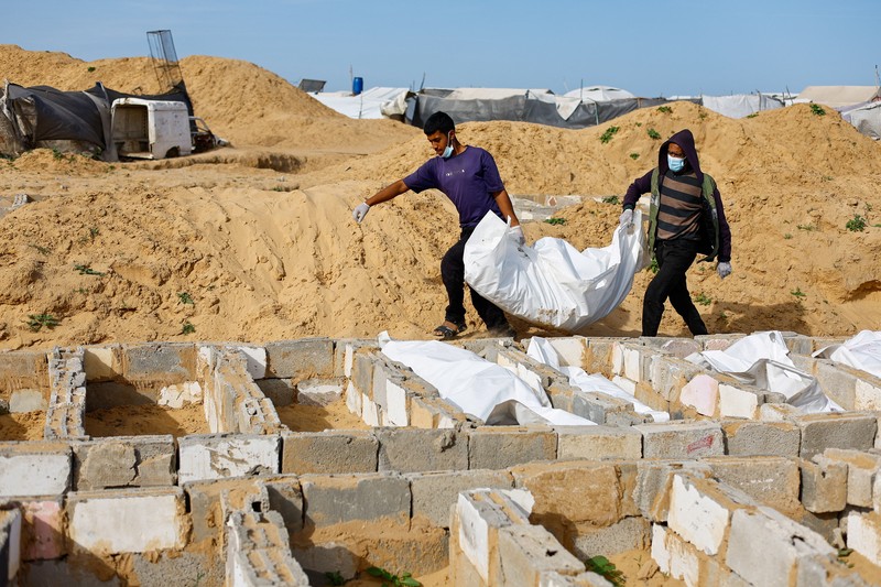 A man gestures next to bodies placed in graves during a mass burial of unidentified Palestinians, whose bodies were released after being held in Israel during the war, in Deir Al-Balah, in the central Gaza Strip, February 13, 2026. REUTERS/Mahmoud Issa