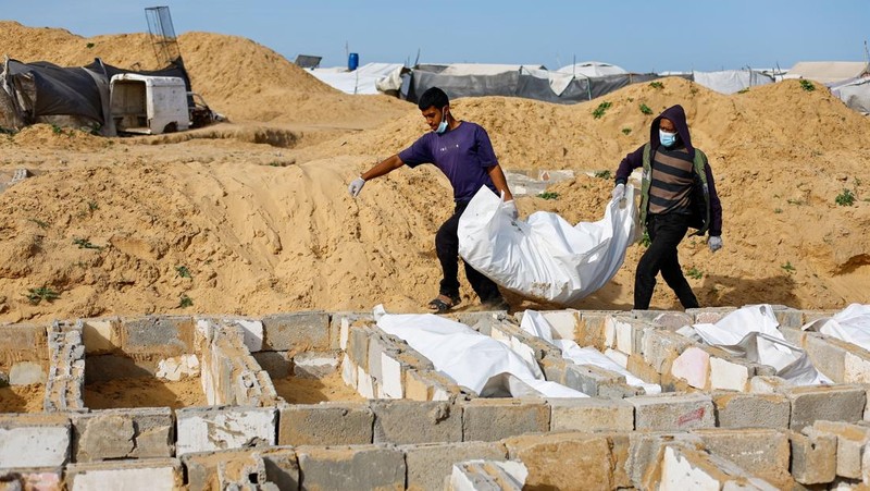 A man gestures next to bodies placed in graves during a mass burial of unidentified Palestinians, whose bodies were released after being held in Israel during the war, in Deir Al-Balah, in the central Gaza Strip, February 13, 2026. REUTERS/Mahmoud Issa