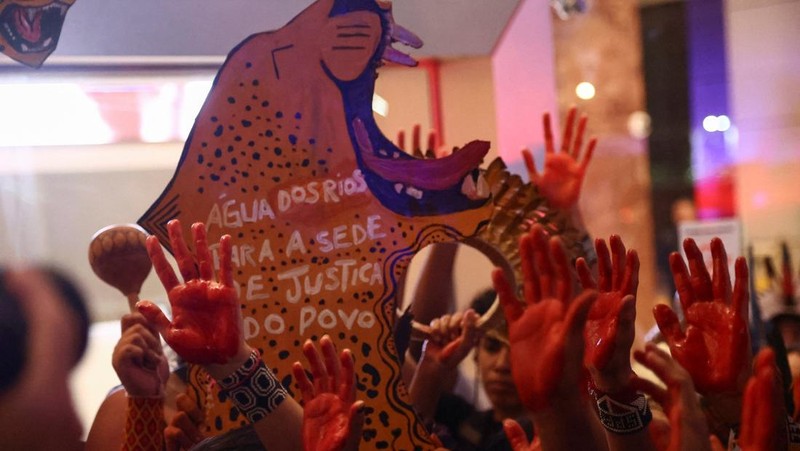 Para pengunjuk rasa menampilkan tanda-tanda saat mereka berdemonstrasi di kantor Cargill untuk mendukung kelompok-kelompok masyarakat adat yang telah memblokir lalu lintas truk selama beberapa hari di pintu masuk terminal Santarem milik Cargill di Brasil utara, memprotes rencana pengerukan sungai Tapajos dan memindahkan lebih banyak biji-bijian seperti kedelai dan jagung yang ditujukan untuk pasar ekspor, di Sao Paulo, Brasil, 20 Februari 2026. (REUTERS/Jean Carniel)