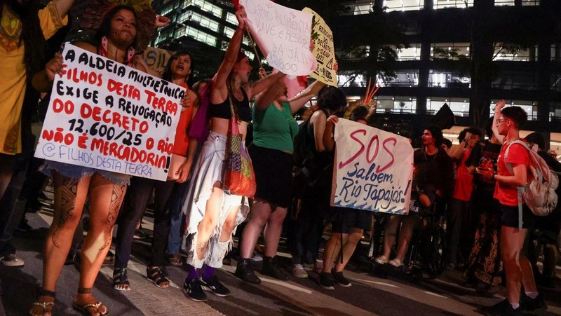 Para pengunjuk rasa menampilkan tanda-tanda saat mereka berdemonstrasi di kantor Cargill untuk mendukung kelompok-kelompok masyarakat adat yang telah memblokir lalu lintas truk selama beberapa hari di pintu masuk terminal Santarem milik Cargill di Brasil utara, memprotes rencana pengerukan sungai Tapajos dan memindahkan lebih banyak biji-bijian seperti kedelai dan jagung yang ditujukan untuk pasar ekspor, di Sao Paulo, Brasil, 20 Februari 2026. (REUTERS/Jean Carniel)