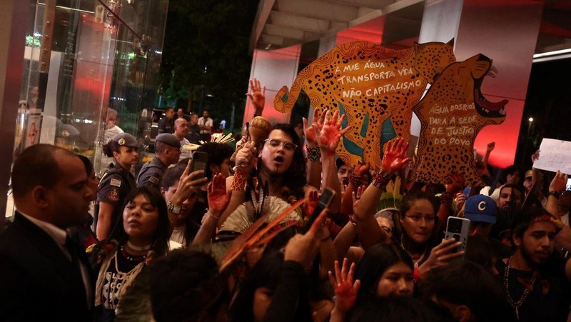 Para pengunjuk rasa menampilkan tanda-tanda saat mereka berdemonstrasi di kantor Cargill untuk mendukung kelompok-kelompok masyarakat adat yang telah memblokir lalu lintas truk selama beberapa hari di pintu masuk terminal Santarem milik Cargill di Brasil utara, memprotes rencana pengerukan sungai Tapajos dan memindahkan lebih banyak biji-bijian seperti kedelai dan jagung yang ditujukan untuk pasar ekspor, di Sao Paulo, Brasil, 20 Februari 2026. (REUTERS/Jean Carniel)