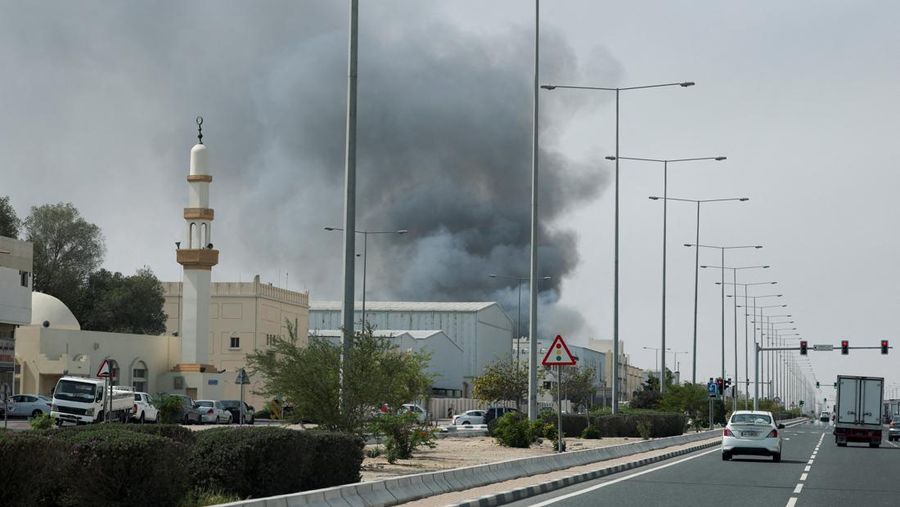 Para pengendara melintas di dekat kepulan asap yang dilaporkan berasal dari serangan Iran di distrik industri Doha, Minggu (1/3/2026). (AFP/MAHMUD HAMS)