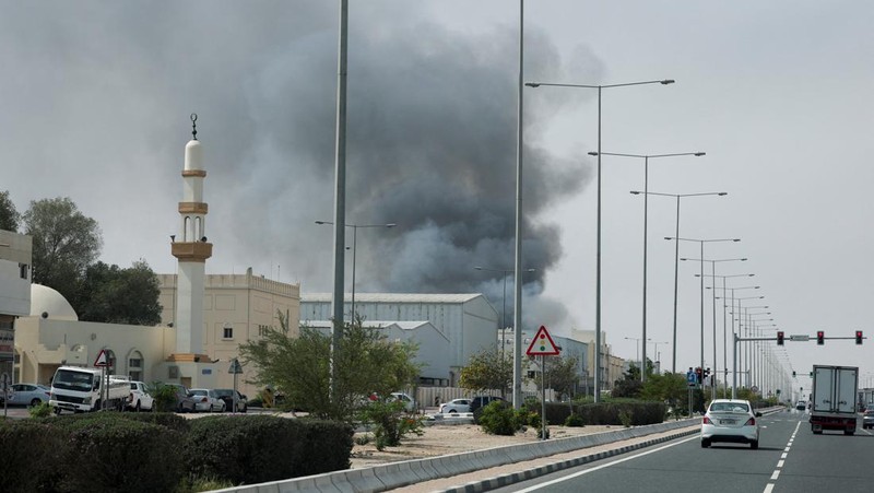 Para pengendara melintas di dekat kepulan asap yang dilaporkan berasal dari serangan Iran di distrik industri Doha, Minggu (1/3/2026). (AFP/MAHMUD HAMS)