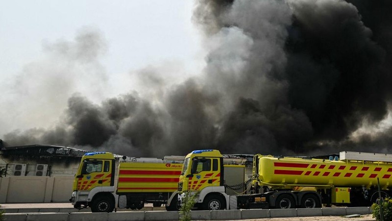 Para pengendara melintas di dekat kepulan asap yang dilaporkan berasal dari serangan Iran di distrik industri Doha, Minggu (1/3/2026). (AFP/MAHMUD HAMS)