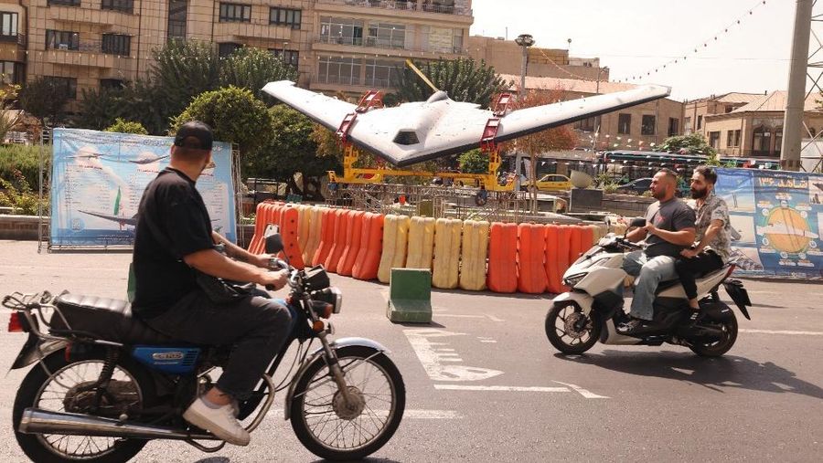 Warga Iran mengendarai sepeda motor mereka melewati drone Shahed di Lapangan Baharestan Teheran pada 27 September 2025, sebagai bagian dari pameran untuk menandai 