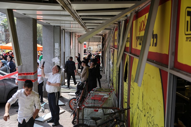 People gather near destroyed vehicles following an Iranian projectile strike, amid the U.S.-Israeli conflict with Iran, in central Israel, March 15, 2026. REUTERS/Tyrone Siu
