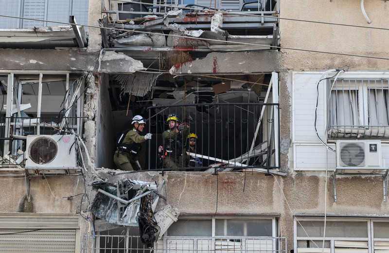 People gather near destroyed vehicles following an Iranian projectile strike, amid the U.S.-Israeli conflict with Iran, in central Israel, March 15, 2026. REUTERS/Tyrone Siu