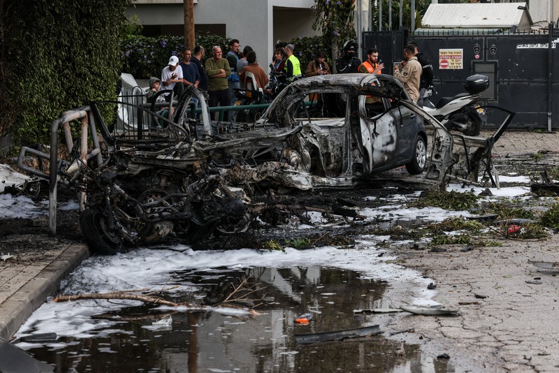 People gather near destroyed vehicles following an Iranian projectile strike, amid the U.S.-Israeli conflict with Iran, in central Israel, March 15, 2026. REUTERS/Tyrone Siu