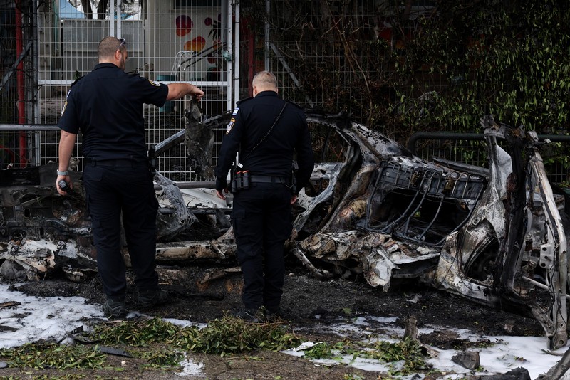 People gather near destroyed vehicles following an Iranian projectile strike, amid the U.S.-Israeli conflict with Iran, in central Israel, March 15, 2026. REUTERS/Tyrone Siu