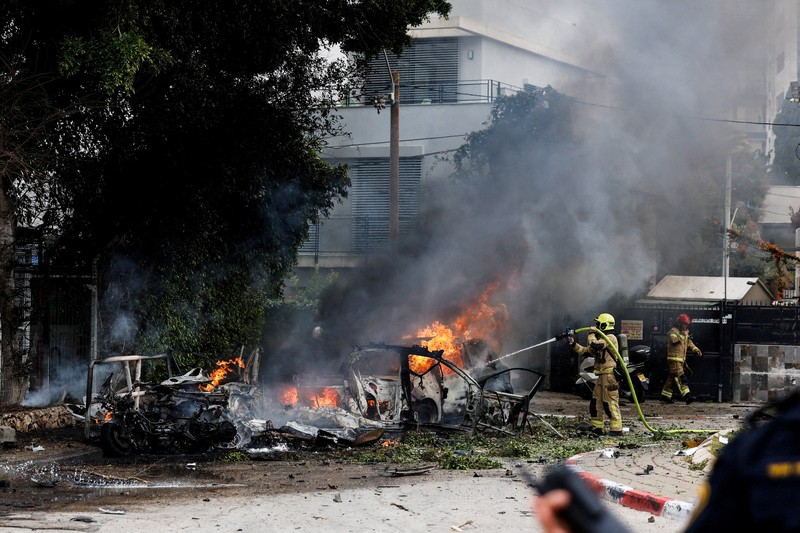 People gather near destroyed vehicles following an Iranian projectile strike, amid the U.S.-Israeli conflict with Iran, in central Israel, March 15, 2026. REUTERS/Tyrone Siu