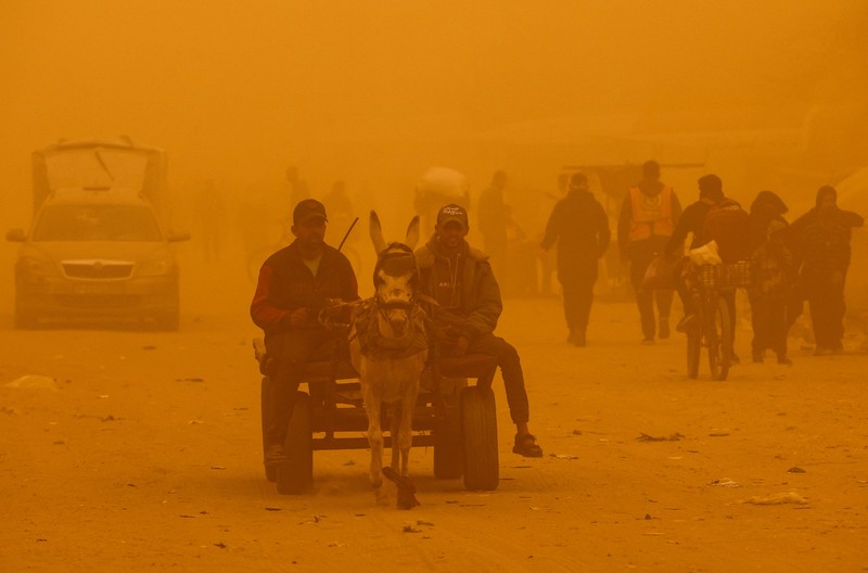 Palestinians walk amid a sandstorm in a tent camp sheltering Palestinians displaced during the two-year Israeli offensive, in Khan Younis in the southern Gaza Strip, March 14, 2026. REUTERS/Ramadan Abed