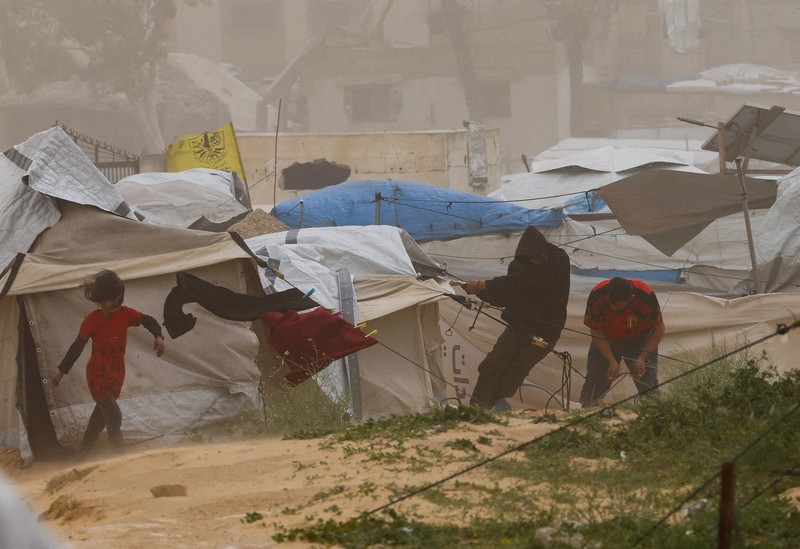 Palestinians walk amid a sandstorm in a tent camp sheltering Palestinians displaced during the two-year Israeli offensive, in Khan Younis in the southern Gaza Strip, March 14, 2026. REUTERS/Ramadan Abed