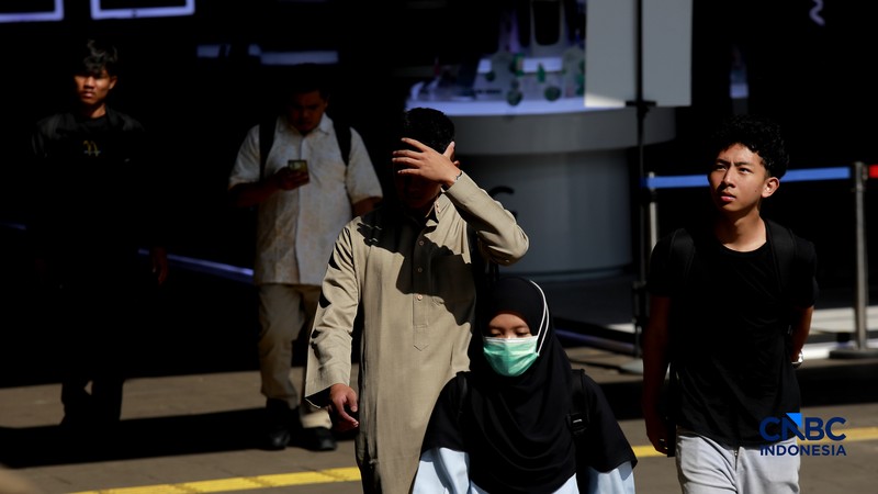 Warga berjalan dengan menutup kepala untuk berlindung dari terik matahari di kawasan Dukuh Atas, Jakarta, Selasa (17/3/2026). (CNBC Indonesia/Muhammad Sabki)