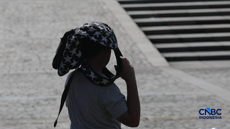 Warga berjalan dengan menutup kepala untuk berlindung dari terik matahari di kawasan Dukuh Atas, Jakarta, Selasa (17/3/2026). (CNBC Indonesia/Muhammad Sabki)