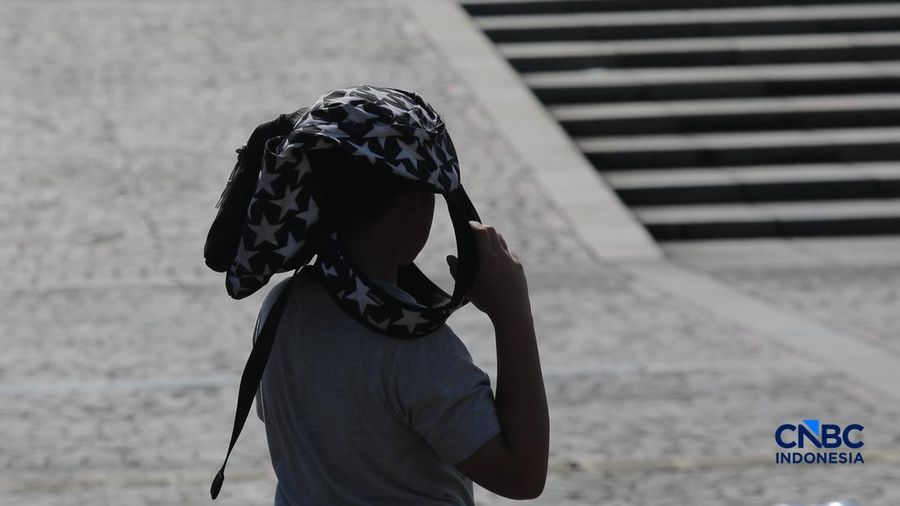 Warga berjalan dengan menutup kepala untuk berlindung dari terik matahari di kawasan Dukuh Atas, Jakarta, Selasa (17/3/2026). (CNBC Indonesia/Muhammad Sabki)