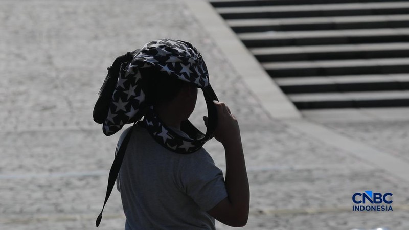 Warga berjalan dengan menutup kepala untuk berlindung dari terik matahari di kawasan Dukuh Atas, Jakarta, Selasa (17/3/2026). (CNBC Indonesia/Muhammad Sabki)