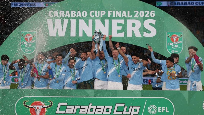 Para pemain Manchester City, termasuk Erling Haaland, Ruben Dias, dan Rodri, merayakan kemenangan dengan mengangkat trofi Piala Carabao di podium setelah final melawan Arsenal di Stadion Wembley, London, Inggris, 22 Maret 2026. (Action Images via Reuters/Paul Childs)