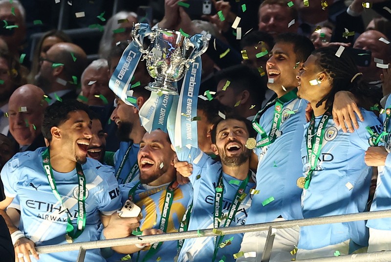 Para pemain Manchester City, termasuk Erling Haaland, Ruben Dias, dan Rodri, merayakan kemenangan dengan mengangkat trofi Piala Carabao di podium setelah final melawan Arsenal di Stadion Wembley, London, Inggris, 22 Maret 2026. (Action Images via Reuters/Paul Childs)