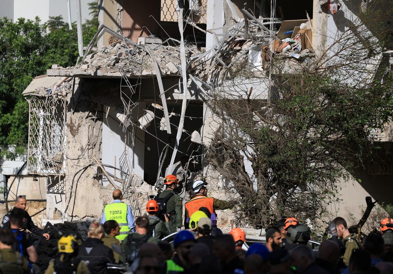 Anggota tim penyelamat bekerja di samping bangunan yang hancur di lokasi kejadian setelah serangan rudal Iran di Israel tengah, di tengah konflik AS-Israel dengan Iran, di Tel Aviv, Israel, Selasa (24/3/2026). (REUTERS/Tomer Appelbaum)